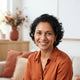 A friendly, diverse middle-aged woman smiling warmly in a bright, modern indoor setting.
